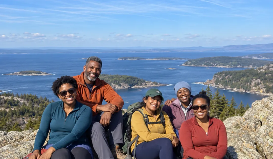 Five hikers resting on a rocky summit above the water